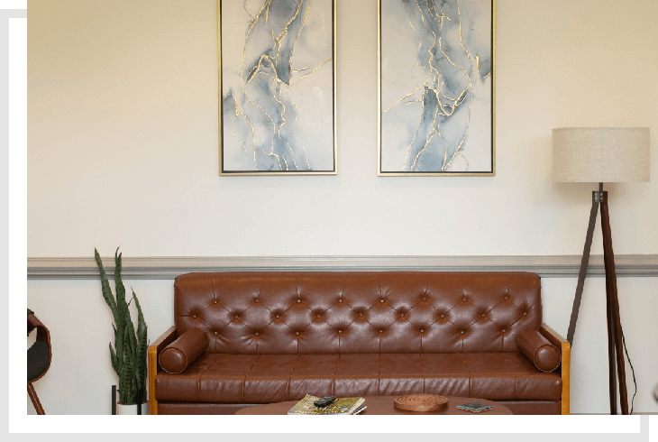 A brown leather couch in front of two paintings.