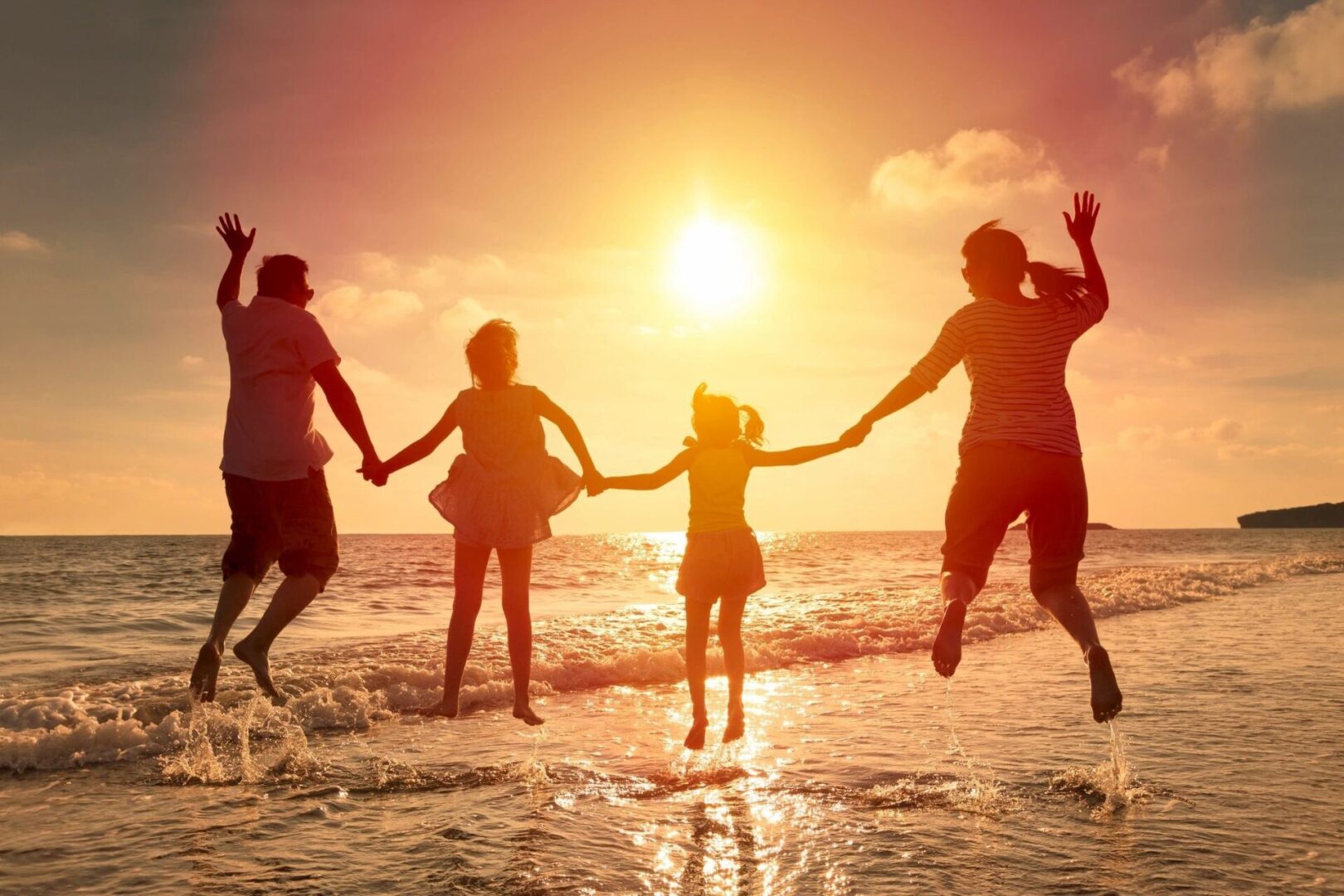 A group of people jumping in the water at sunset.